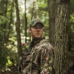 man in brown and green camouflage jacket standing near tree during daytime